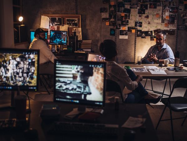 Detectives in a dimly lit room reviewing evidence and discussing a case.