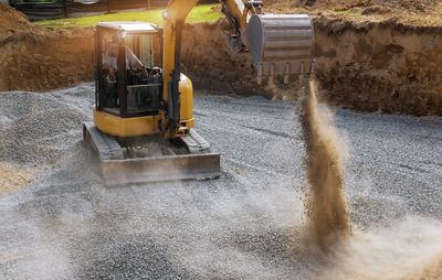 Excavator dumping soil into a gravel-filled construction site.