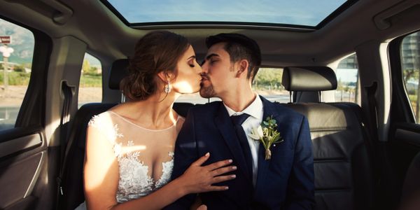 Newlywed couple sharing a romantic kiss inside a car.