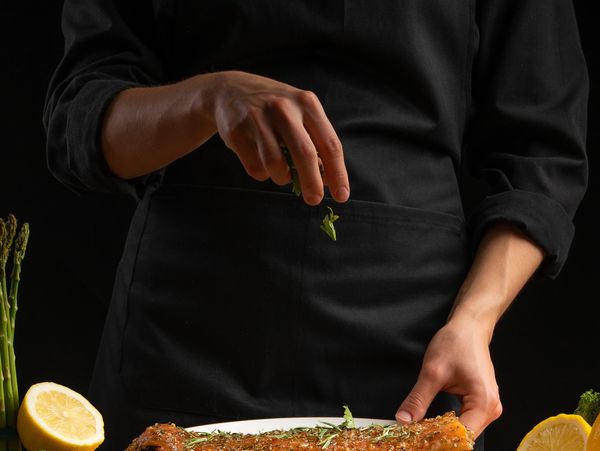 Chef seasoning a fillet of salmon with herbs on a plate.