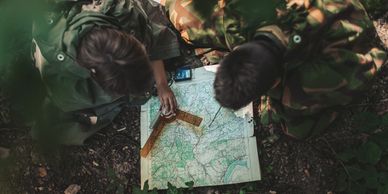 Two people studying a map outdoors, dressed in camouflage and green jackets.