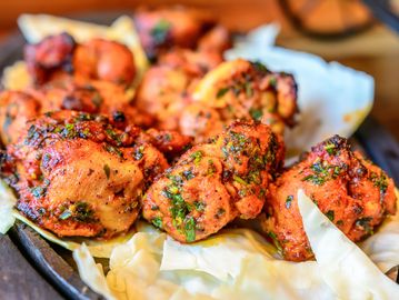 Spicy grilled chicken pieces garnished with herbs on cabbage leaves.