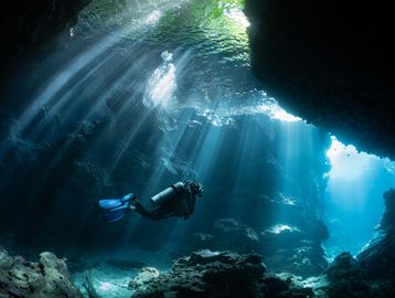A scuba diver explores an underwater cave illuminated by sun rays.