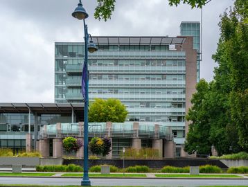 Modern glass building with greenery and hanging flower baskets on a cloudy day.