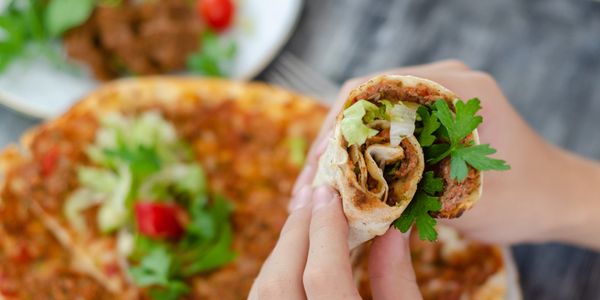 Hands holding a rolled wrap filled with meat and greens.