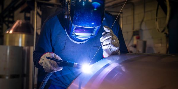 Person welding metal in a workshop with protective gear.