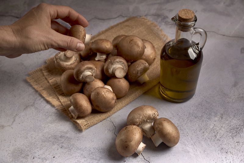 group of portobello mushrooms on a raffia cloth next to an oil jar