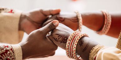 Close-up of couple holding hands adorned with henna and traditional jewelry.