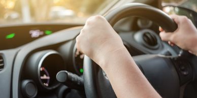 Hands gripping a steering wheel while driving at sunset.