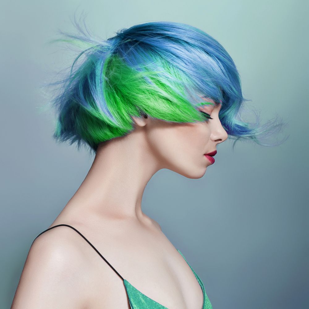 Woman with vibrant blue and green short hair in profile.