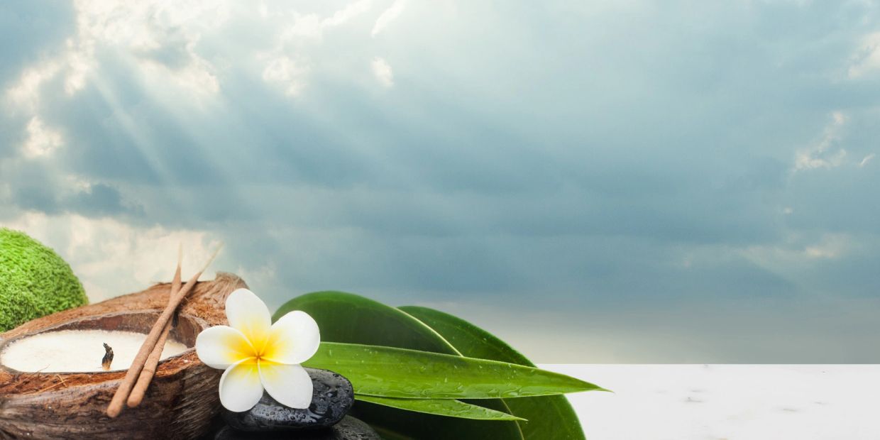Spa elements with candle, incense sticks, flower, and leaves against a cloudy sky.