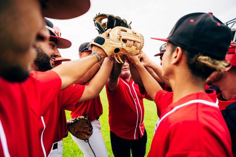 Young Hispanic baseball team and coach raising gloves for motivational high-five before game starts.