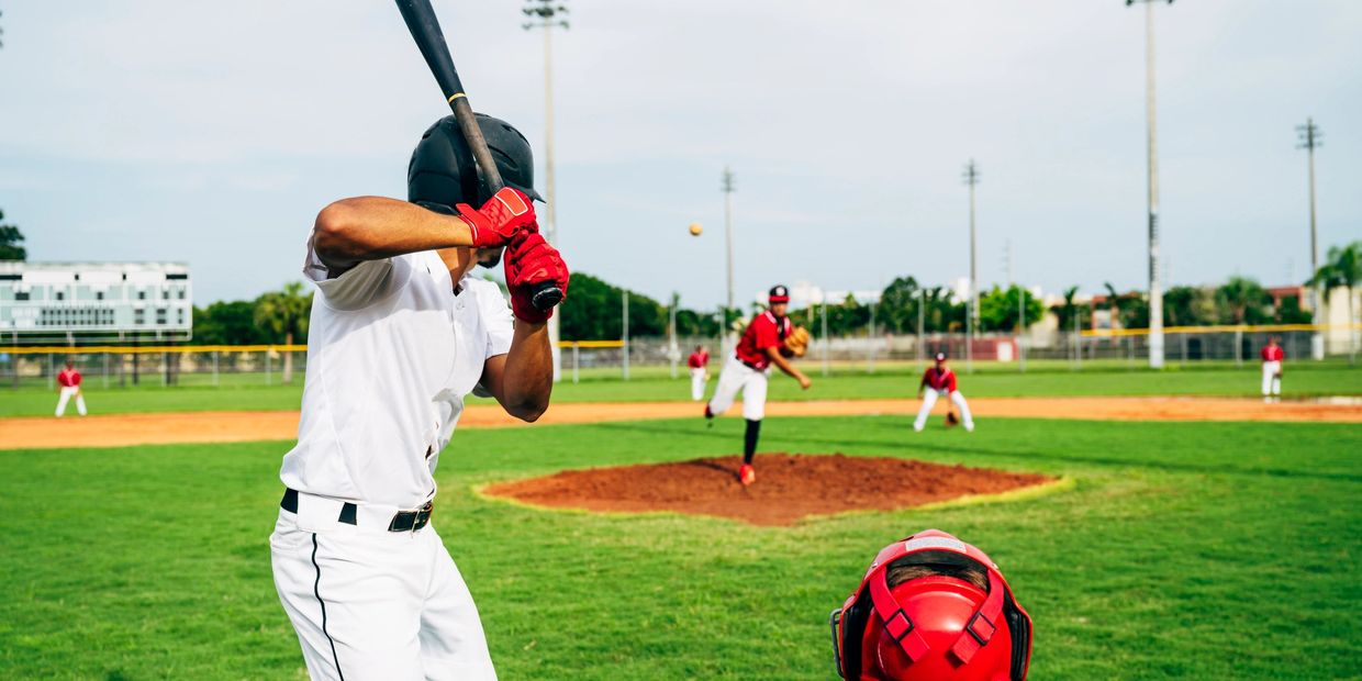 Baseball pitcher throws ball to batter with catcher ready behind home plate.