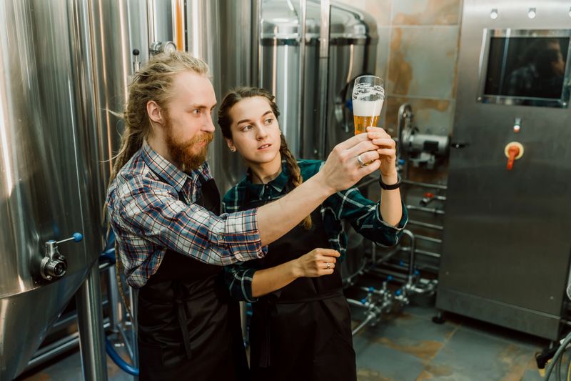 Brewery workers looking at freshly made beer in glass tube and discussing it. Male and female brewer testing beer at brewery factory. 4k.