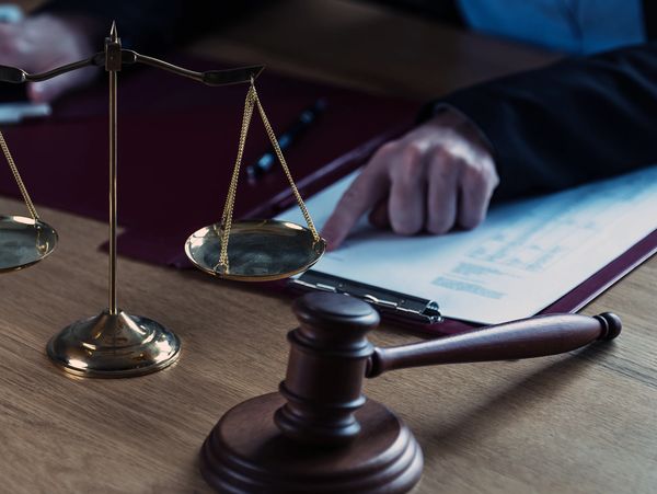 Legal symbols including scales of justice and gavel on a desk with a person reviewing documents.