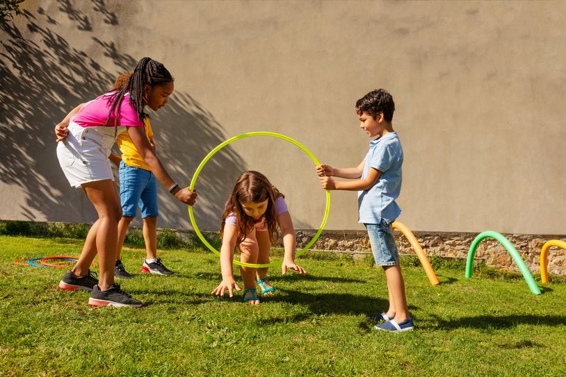 Children playing with hoops outdoors on grass in sunny weather.