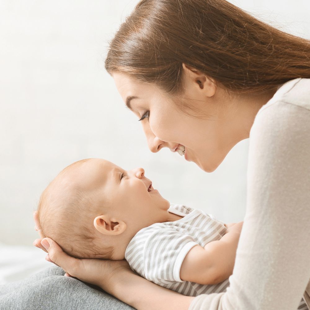 Mother lovingly gazes at smiling baby in her arms.
