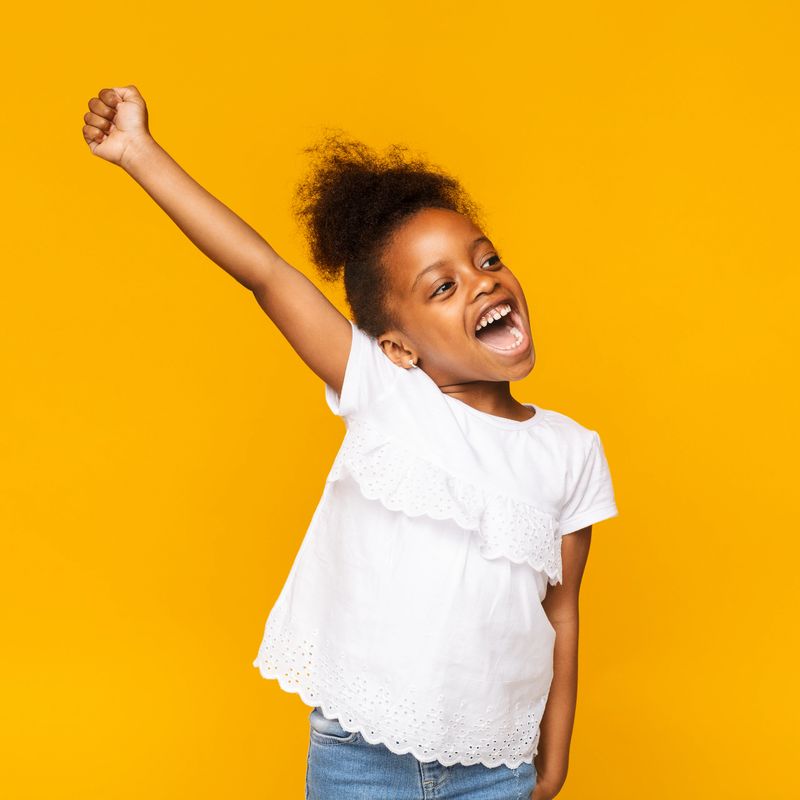 Dream come true. Cute african toddler girl shouting hooray, gesturing hand up on orange studio background