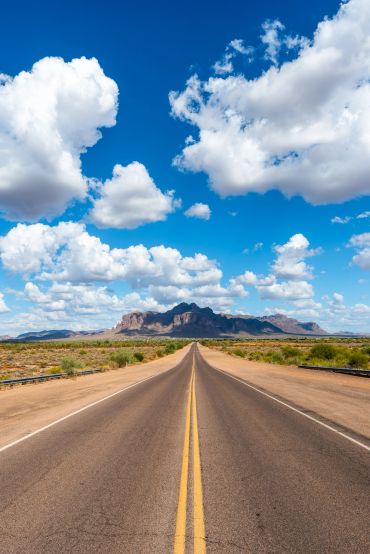 Empty road leading to distant mountains under a blue sky with clouds.