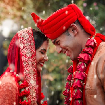 Bride and groom in traditional wedding attire smiling at each other.