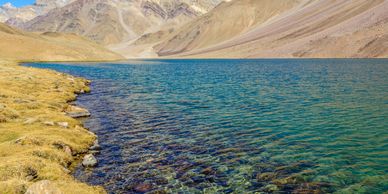Clear blue lake surrounded by barren mountains under a bright sky.