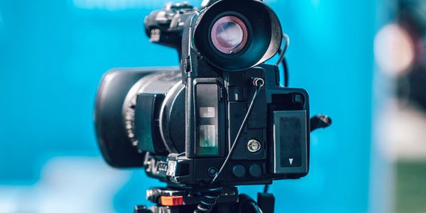 Close-up of a professional video camera on a tripod with a blue background.