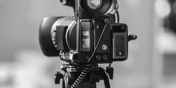 Close-up of a professional video camera on a tripod with a blue blurred background.