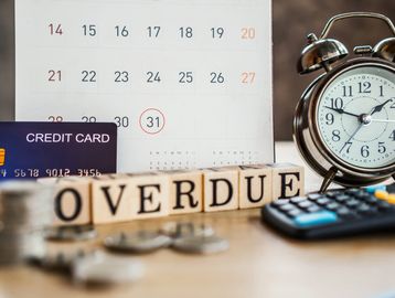 Wooden blocks spell 'OVERDUE' with a credit card, coins, calendar, clock, and calculator.