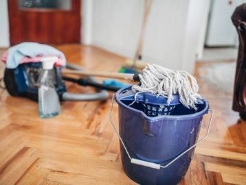 Bucket with mop and cleaning supplies on wooden floor.