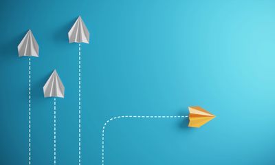 Yellow paper plane diverging from white ones on a blue background.