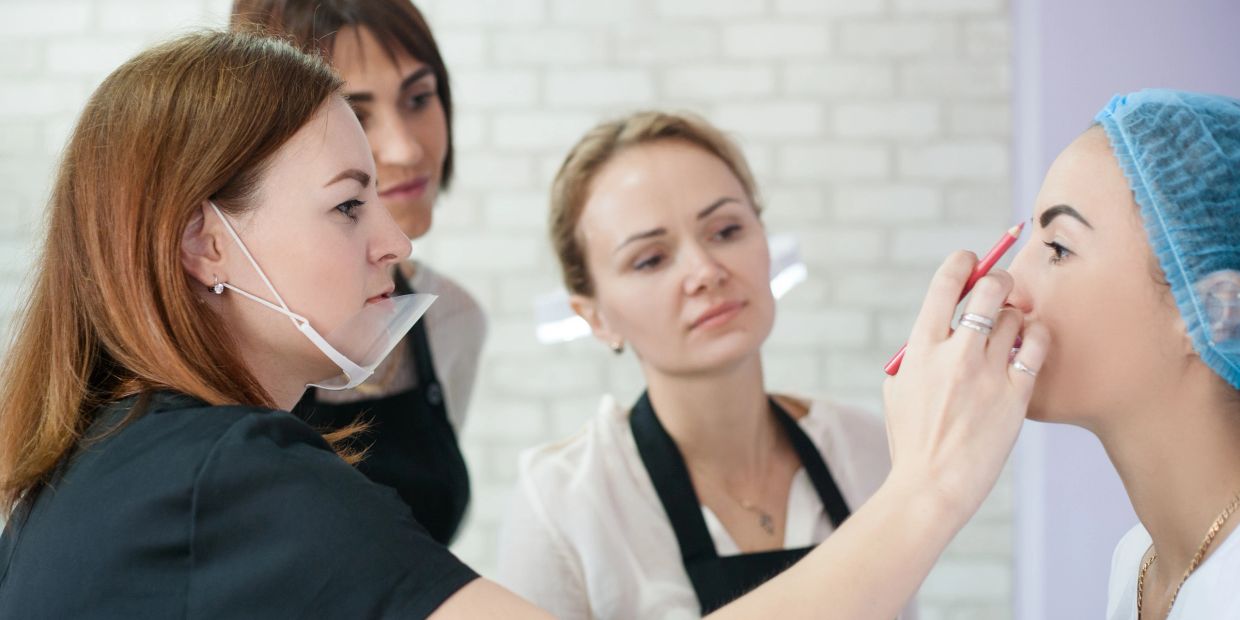 A makeup artist demonstrates eyebrow shaping on a model while others observe.
