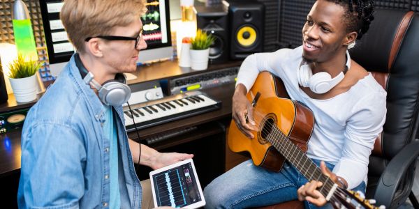 Two musicians collaborating in a studio with guitar and tablet.