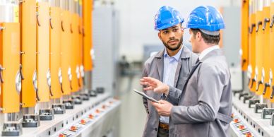 Two engineers discussing at an industrial control panel.