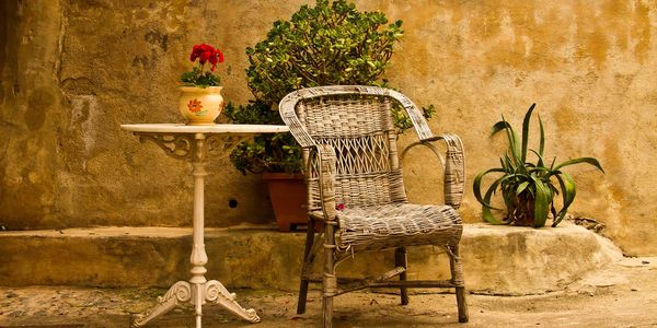 Rustic wicker chair and white table with a potted red flower against a textured wall.
