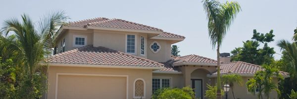 A brick house with a palm tree and cars parked outside.