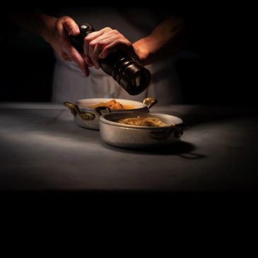 Person grinding pepper on food in a dimly lit setting.