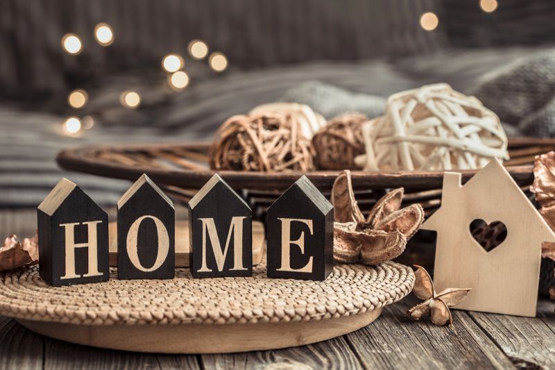 Still life with objects of festive home decor and wooden letters with the inscription home, near a small wooden house.