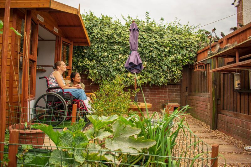 Authentic Disabled Female in Wheelchair With Asian Caregiver, Carer. Real, Healthcare, Feeding Birds In Her Own Garden.
