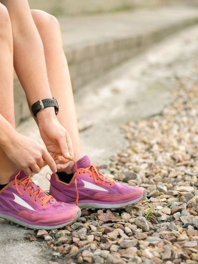 Person tying shoelaces on purple running shoes outdoors.