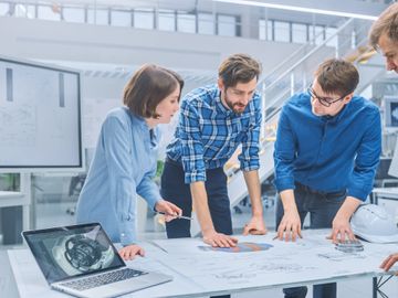 Four engineers collaborate over technical blueprints in a modern workspace.