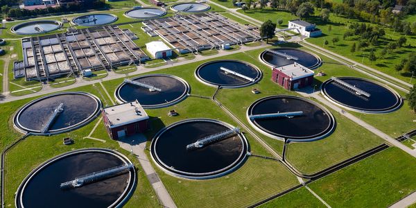 Aerial view of a large wastewater treatment plant with circular clarifiers and green surroundings.