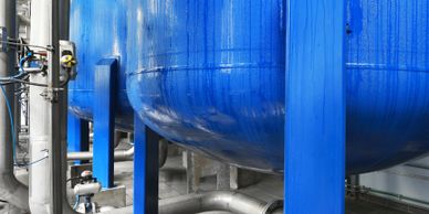 Large blue industrial tanks supported by blue metal beams in a factory setting.