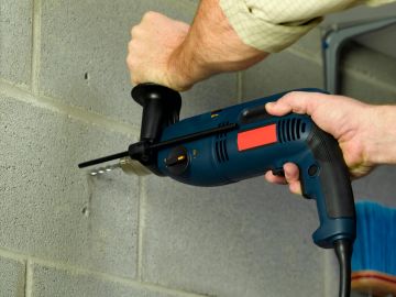 Person using a power drill on a concrete block wall.