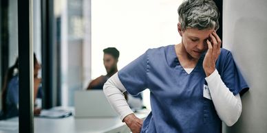 Tired nurse leaning against wall, looking stressed.