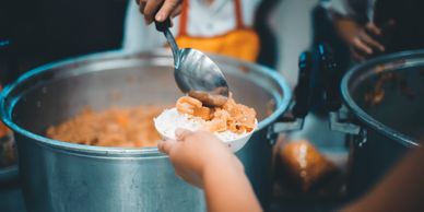 Serving food from a large pot into a bowl of rice.