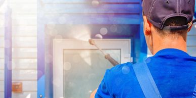 Man power washing a glass door on a sunny day.