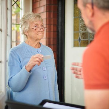 Elderly woman handing over a card to a delivery man at the door.
