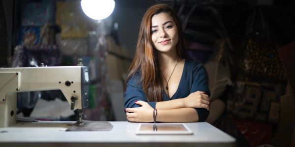 Young woman sitting at a sewing machine with a tablet.