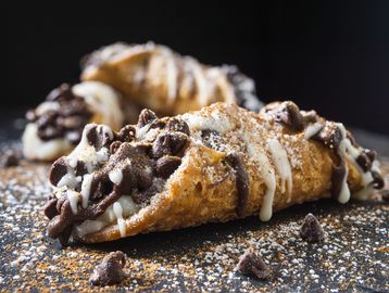 Classic Italian cannoli filled with sweet ricotta and chocolate chips, dusted with powdered sugar.