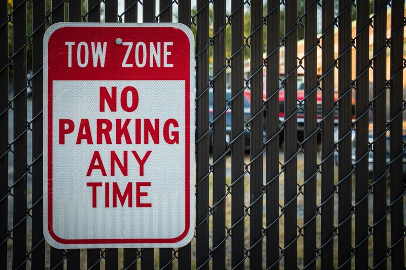 Tow Zone No Parking sign on black fence warns people away from parking lot